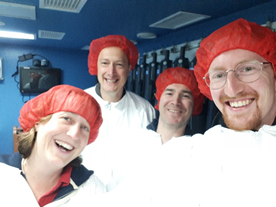 Four scientists wearing red hairnets and white plastic coats